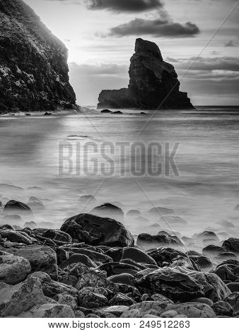 Evening Bay. Sharp Rocks, Black Rounded Boulders, Stony Beach, Sand And Dark Sky.