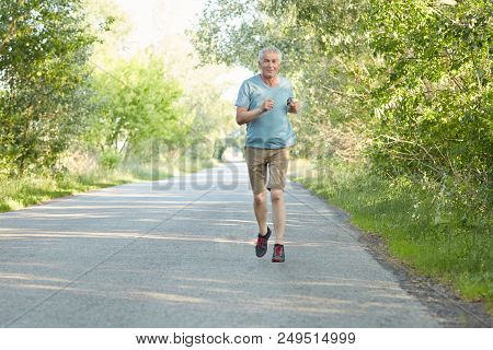Horizontal Shot Of Active Senior Male Runs On Asphalt Very Quickly, Dressed In Spotswear, Goes In Fo
