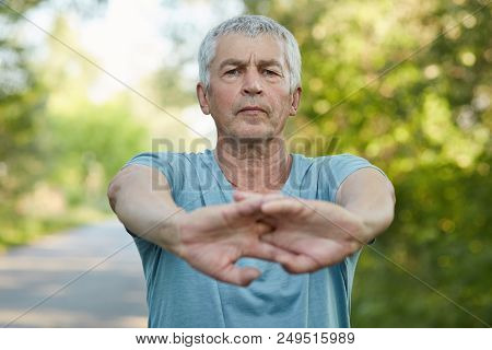 Serious Wrinkled Grey Haired Male Stretches Hands With Confident Facial Expression, Dressed Casually