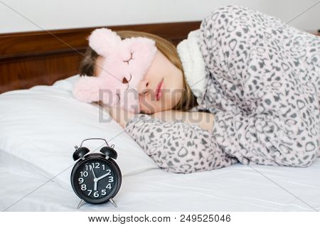 Young Woman Girl In Cute Sleep Mask And Warm Pajamas Sleep With Alarm Clock On The Bed In The Mornin