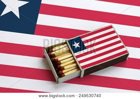 Liberia Flag  Is Shown In An Open Matchbox, Which Is Filled With Matches And Lies On A Large Flag.