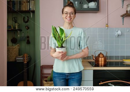 Horizontal Shot Of Young Positive European Caucasian Lady Standing In Her Kitchen In Casual Clothes 