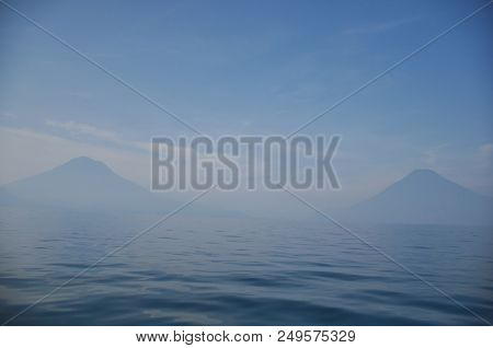 Lake Atitlan In Early Morning Haze With San Pedro Volcano And Atitlan Volcano In The Background