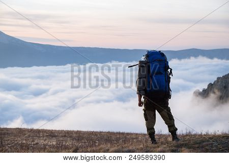 A Tourist Is Standing In The Mountains With A Backpack And Looking At The Clouds. Demerdzhi, Crimea.