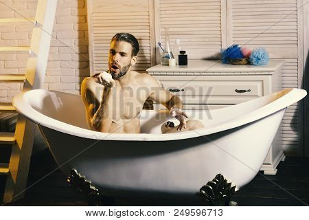 Man With Beard Taking Bath And Blowing Foam. Sexuality And Relaxation Concept. Macho Sitting Naked I
