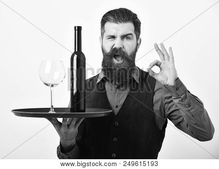 Man With Beard Holds Bottle With Alcohol On White Background. Waiter With Glass And Bottle Of Wine O