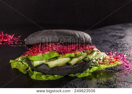 Healthy Black Bun Burger With Cucumbers, Avocade And Sprouts On Dark Background.