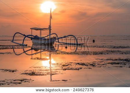 A Balinesian Fishing Boat At Sunrise, Reflections In The Shallow Sea, Sanur, Bali, Indonesia, April 