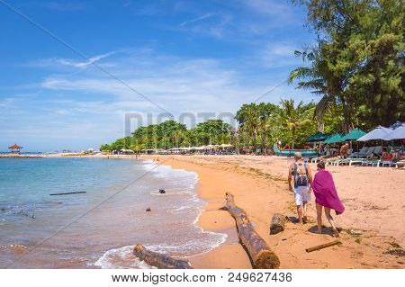 A Balinese Beach With Sunbeds And Two Big Timber Logs In The Water, Sanur, Bali, Indonesia, April 21