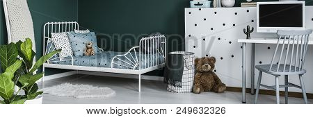 Green Kids Bedroom Interior With Metal Bed, Computer On Desk And Teddy Bear Sitting Next To Patterne