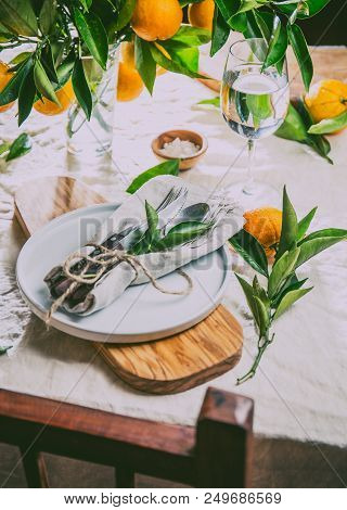 Table Setting With White Plate, Cutlery, Linen Napkin And Orange Tree Branch Decoration On White Lin