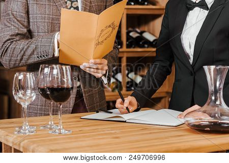 Cropped Shot Of Wine Steward Writing Notes While Customer Making Order At Wine Store