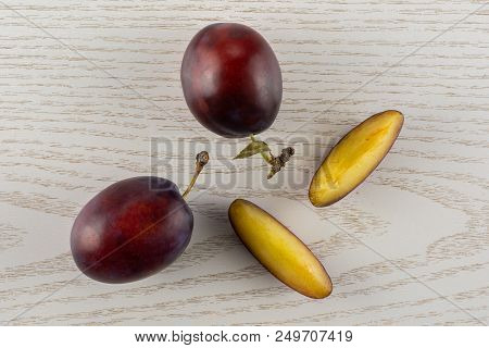 Group Of Two Whole Two Slices Of Fresh Violet-blue Plum Vibrant Moyer Variety Flatlay On Grey Wood