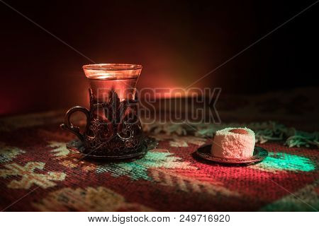 Arabian Tea In Glass With Eastern Snacks On A Carpet On Dark Background With Lights And Smoke. Easte