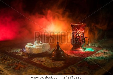 Arabian Tea In Glass With Eastern Snacks On A Carpet On Dark Background With Lights And Smoke. Easte