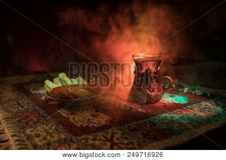 Arabian Tea In Glass With Eastern Snacks On A Carpet On Dark Background With Lights And Smoke. Easte
