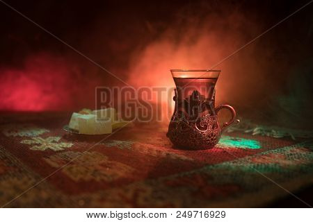 Arabian Tea In Glass With Eastern Snacks On A Carpet On Dark Background With Lights And Smoke. Easte