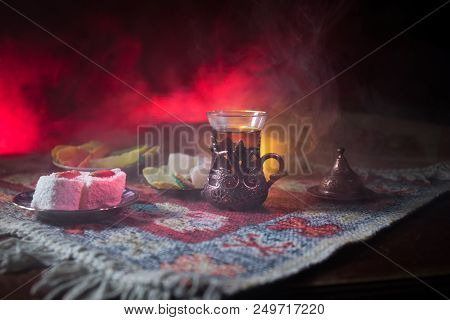 Arabian Tea In Glass With Eastern Snacks On A Carpet On Dark Background With Lights And Smoke. Easte