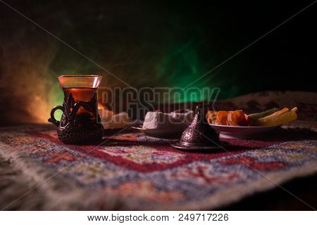 Arabian Tea In Glass With Eastern Snacks On A Carpet On Dark Background With Lights And Smoke. Easte