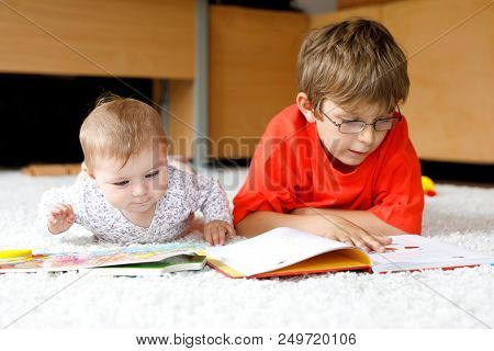 Baby Girl And School Kid Boy Reading Books At Home. Excited Siblings In Nightwear. Brother Child Rea