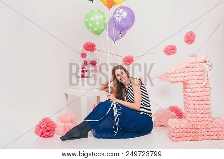 Girl Sitting On The Floor Holding Colored Balloons On A White Background. Beautiful Woman On Holiday