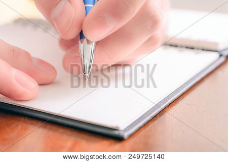 A Macro Of A Male Hand Writing In A Blank Organizer With A Biro