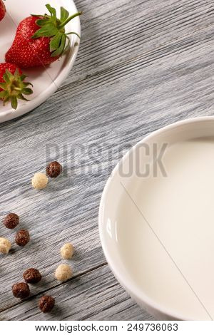 Chocolate and white grain balls with strawberries and of milk plate on a gray wooden table with copy space. Top view