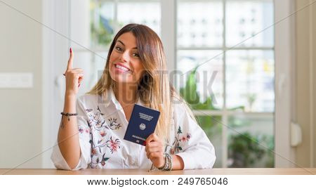 Young woman at home holding a passport of Germany surprised with an idea or question pointing finger with happy face, number one