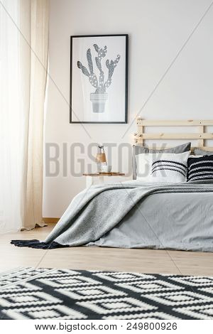 Patterned Carpet And Poster In Grey Simple Bedroom Interior With Blanket On Bed. Real Photo