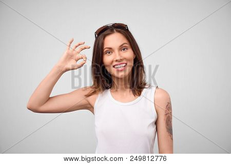 Young European Brunette Woman Showing Ok Gesture With His Fingers. Happy Woman In White Top Smiling 
