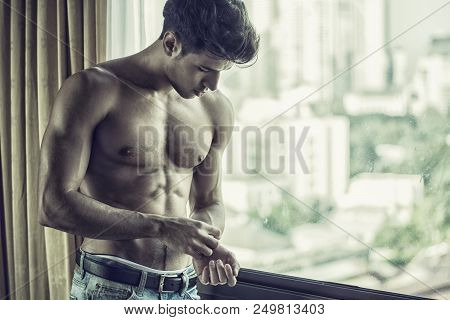 Sexy Handsome Young Man Standing Shirtless In His Bedroom Next To Window Curtains, Adjusting Wrist W
