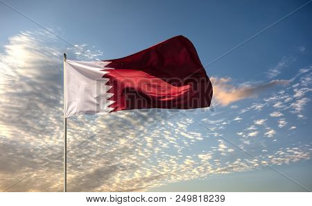 Real Flag Of The Country Qatar Waving In The Wind Against The Background Of A Blue Sky And Clouds.