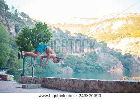 Young Man Doing A Side Flip Or Somersault While Practicing Parkour On A Lake In The Countryside.