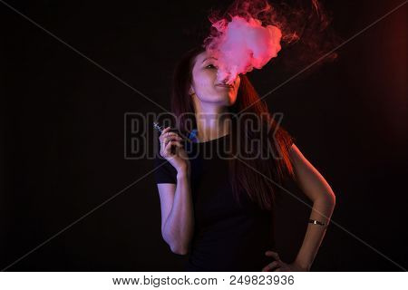 Young Woman In Neon Light And Smoke Of E-cigarettes Or Vape On Black Background.