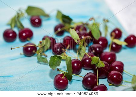 Red Fresh Ripe Cherries With Green Leaves On A Blue Background, Close-up. Summer, Healthy Fruits And