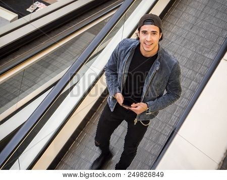 Young Trendy Man On Moving Walkway Or Travellator Or Autowalk, Looking Ata Camera