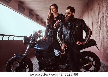 Portrait Of A Brutal Fashionable Biker Dressed In A Black Leather Jacket With Sunglasses Sitting On 