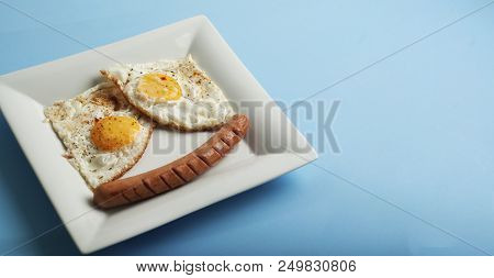 Traditional Clasic Breakfast Fried Eggs And Sausage On A White Square Porcelain Plate. Isoalted On B
