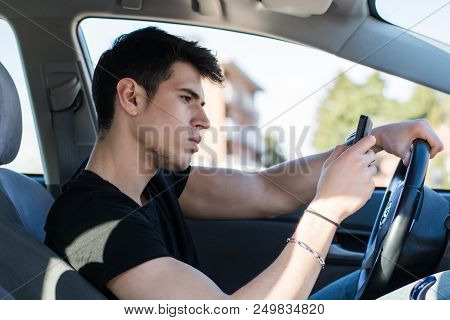 Inattentive Handsome Young Man Busy With His Mobile Phone While Driving A Car.