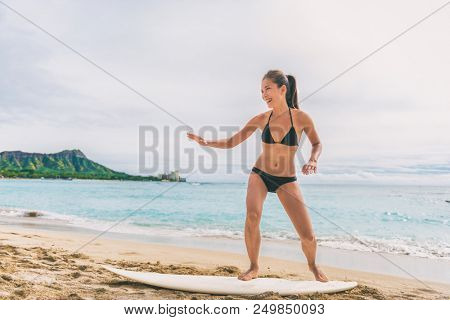 Asian tourist woman on Hawaii beach learning to surf at surfing school in Waikiki, Honolulu, Oahu. Girl having fun practicing on surfboard on shore.