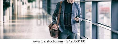 Business man texting on mobile phone commuting walking in airport with messenger bag using cellphone texting sms message on smartphone app - young businessman commute lifestyle panoramic banner.