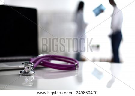 Laptop And Stethoscope On The Desk , Doctors Standing In The Background.