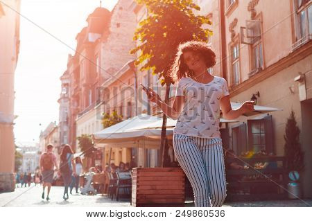 Beautiful Young Girl Using Smartphone And Listening To The Music Walking On Street. Happy Woman Danc
