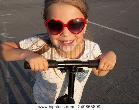 Street Sport: Happy Girl In Riding A Kick Scooter On The Pavement And Puddles. Portrait. Close-up.