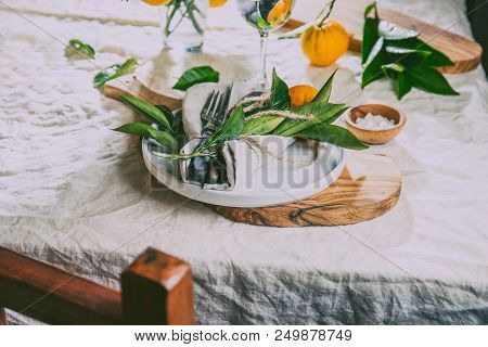 Table Setting With White Plate, Cutlery, Linen Napkin And Orange Tree Branch Decoration On White Lin