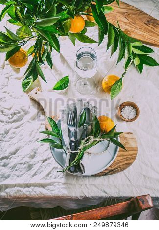 Table Setting With White Plate, Cutlery, Linen Napkin And Orange Tree Branch Decoration On White Lin