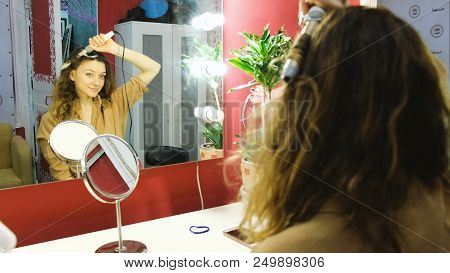 Young Beautiful Girl Looks In The Mirror And Curls Curls On The Curling Iron In The Dressing Room, S