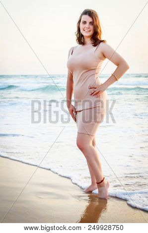 Nice Looking Cute Caucasian Girl In A Long Pink Dress At The Seaside, With Sea Waves On The Backgrou