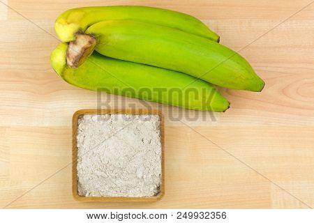 Synbiotic dried banana fruit powder made of organic whole Gros Michel banana, known as Big Mike, top view on wooden background 

