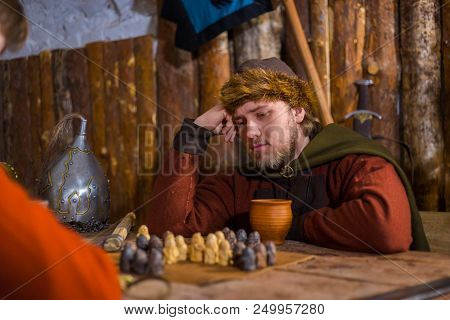 Portrait Of Man In Russian Ethnic Suit Playing Board Game Like Chess. Folk, Competition And Traditio